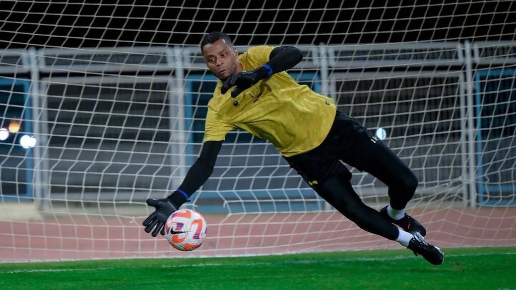 Goleiro Paulo Vitor vestindo uniforme amarelo do Al-Ohkdood Club e realizando defesa durante a partida.