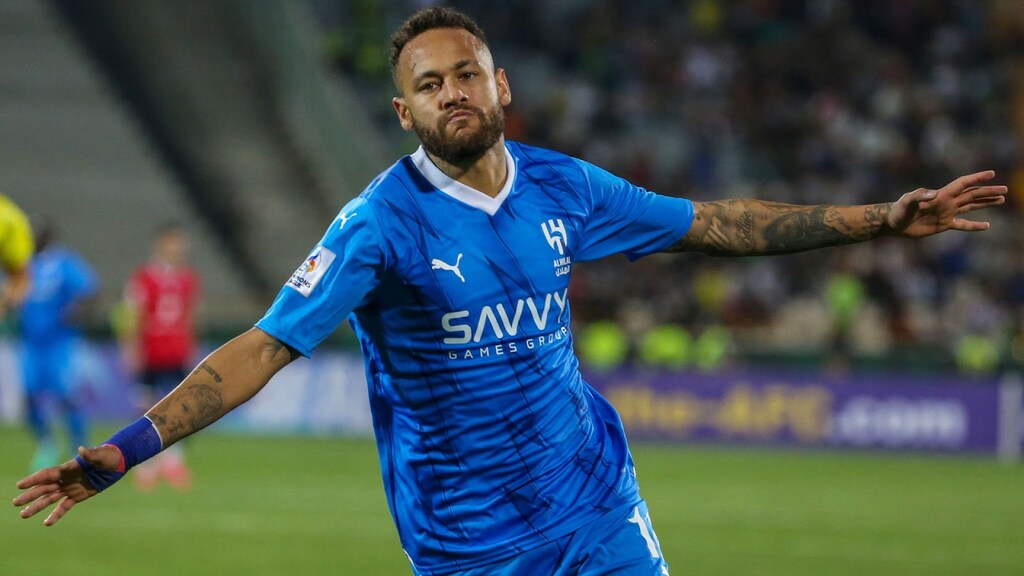 Jogador de futebol, Neymar, vestindo uniforme azul do Al-Hilal e correndo de braços abertos comemorando gol.