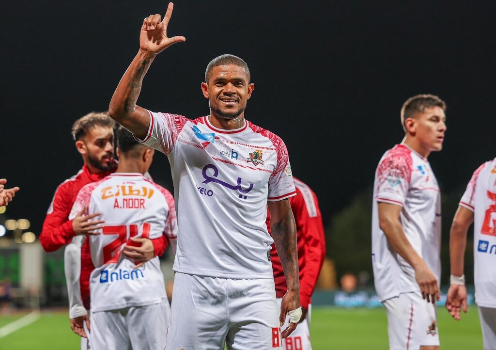 Jogador de futebol Anselmo, vestindo uniforme branco com detalhes vermelhos do Al-Wehda durante partida de futebol.