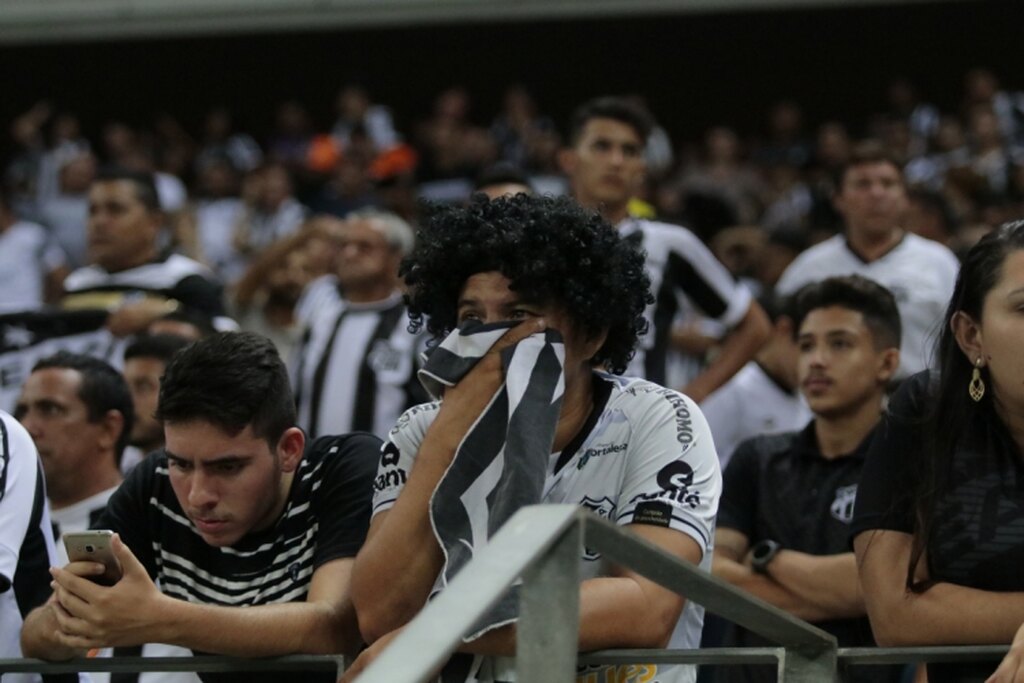 Torcida do Ceará, vestindo uniforme branco e preto do time, chorando no estádio pelo rebaixamento.