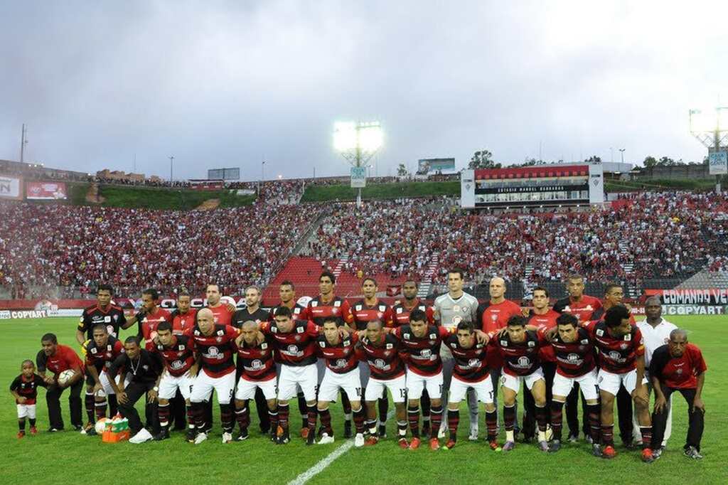 Elenco do Vitória enfileirado para começar a partida com estádio lotado no gramado.