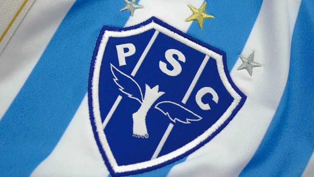 Escudo do Paysandu, bordado no peito de um uniforme azul claro e branco.