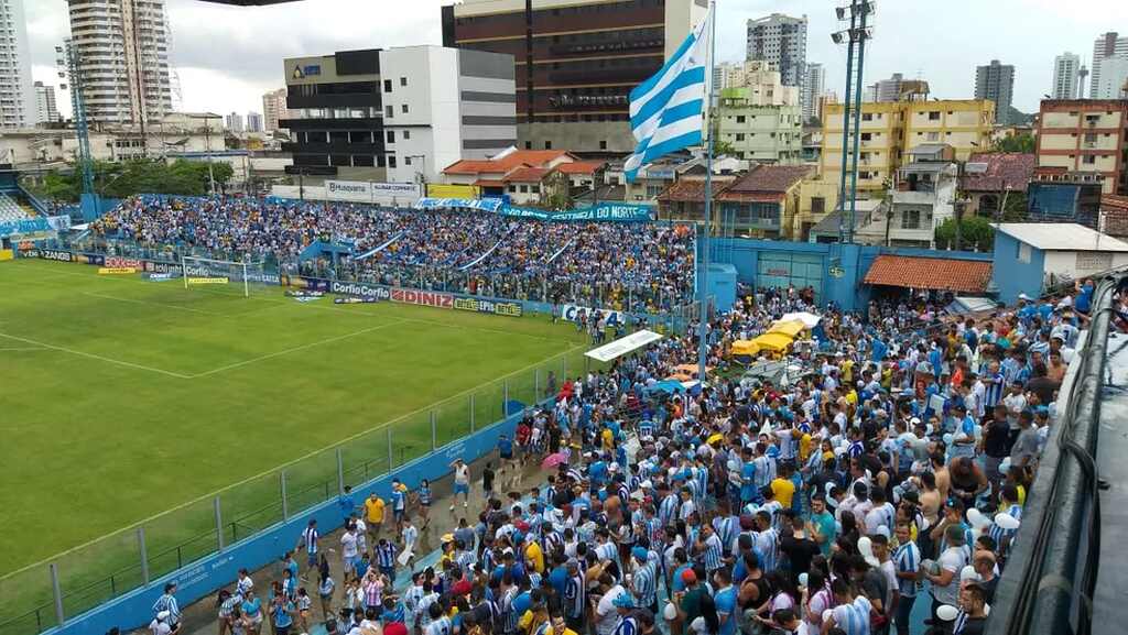 Torcida do Paysandu com uniforme azul e branco, em estádio lotado, durante partida.