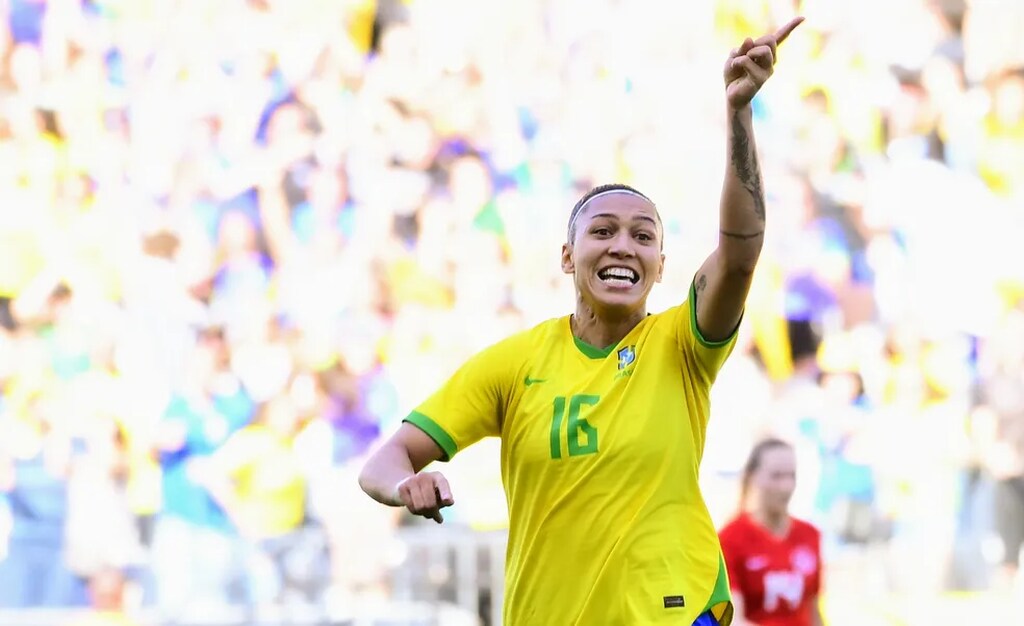 Jogadora da seleção brasileira de futebol, vestindo uniforme amarelo comemorando gol.