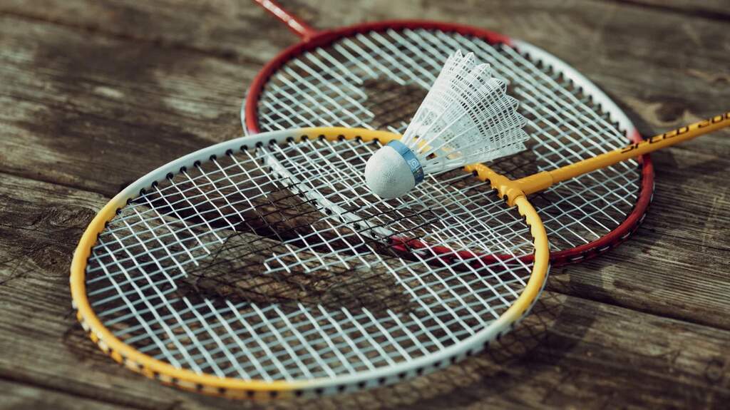 Imagem de duas raquetes de badminton com uma peteca de plástico em cima