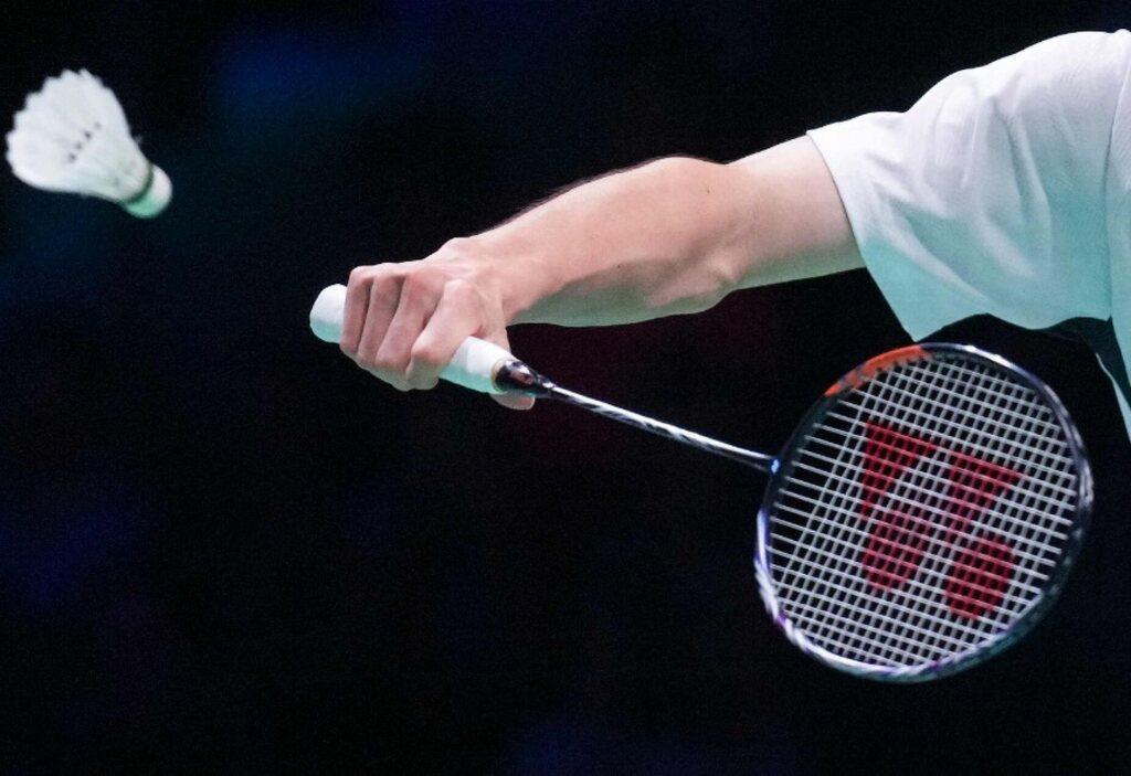 Raquete de badminton erguida por um braço, prestes a rebater uma peteca