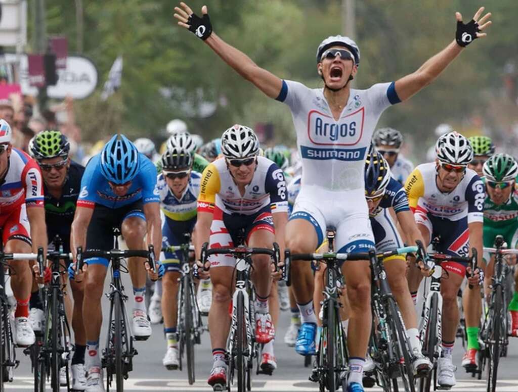 Imagem de atletas de ciclismo de estrada, com um na frente comemorando a vitória