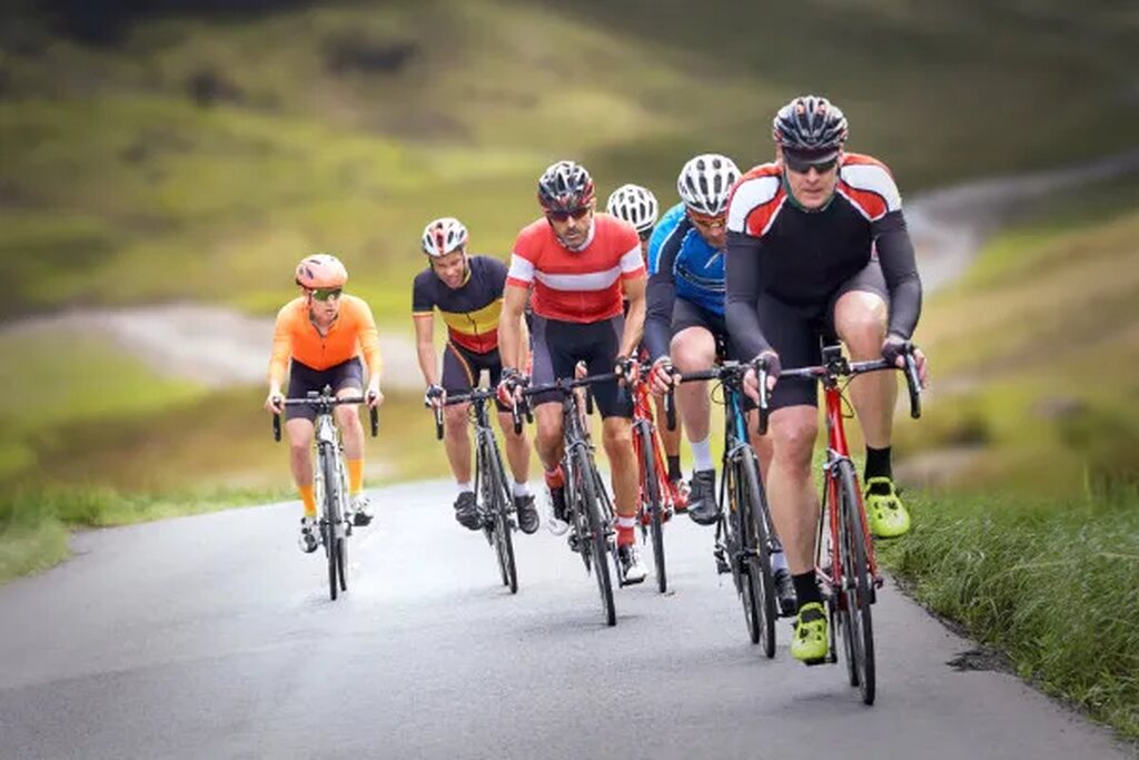 Imagem de pessoas praticando ciclismo na estrada, utilizando capacetes