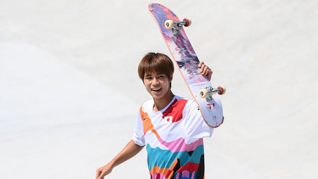 Imagem de Yuto Horigome, medalhista olímpico, comemorando a vitória levantando o skate para o alto e sorrindo