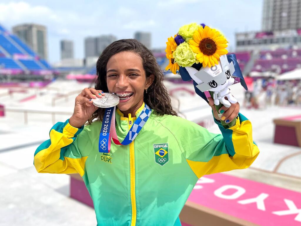 Imagem da atleta brasileira de skate Rayssa Leal, mordendo sua medalha de prata nas olimpíadas e segurando um buquê de flores