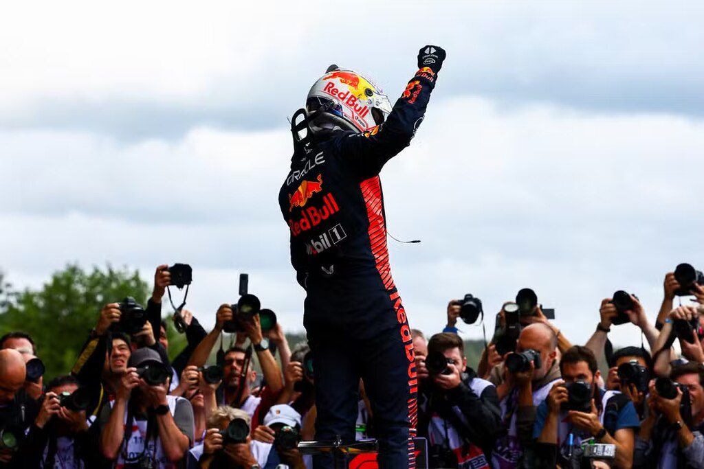 Imagem de um piloto da RedBull comemorando a vitória em frente à imprensa, que o fotografa