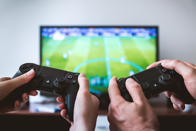 Dois jogadores de esoccer competindo entre si com controles de videogame e em frente a tv