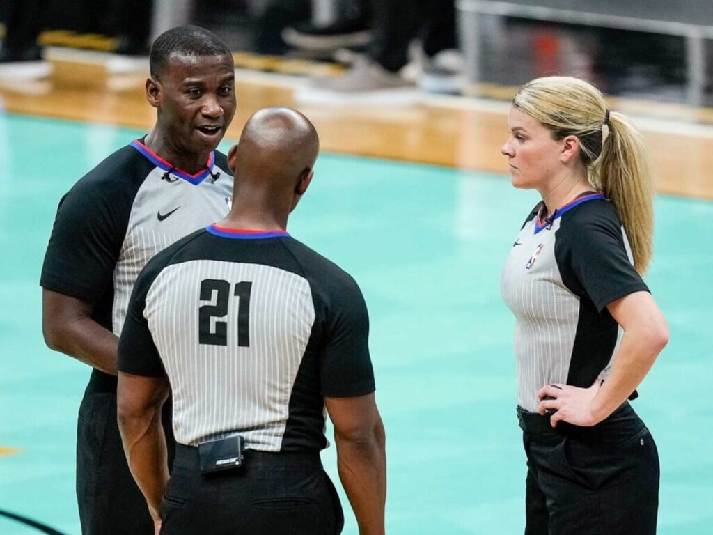 três auxiliares que entendem como a competição de basquete é dirigida conversam entre si na quadra