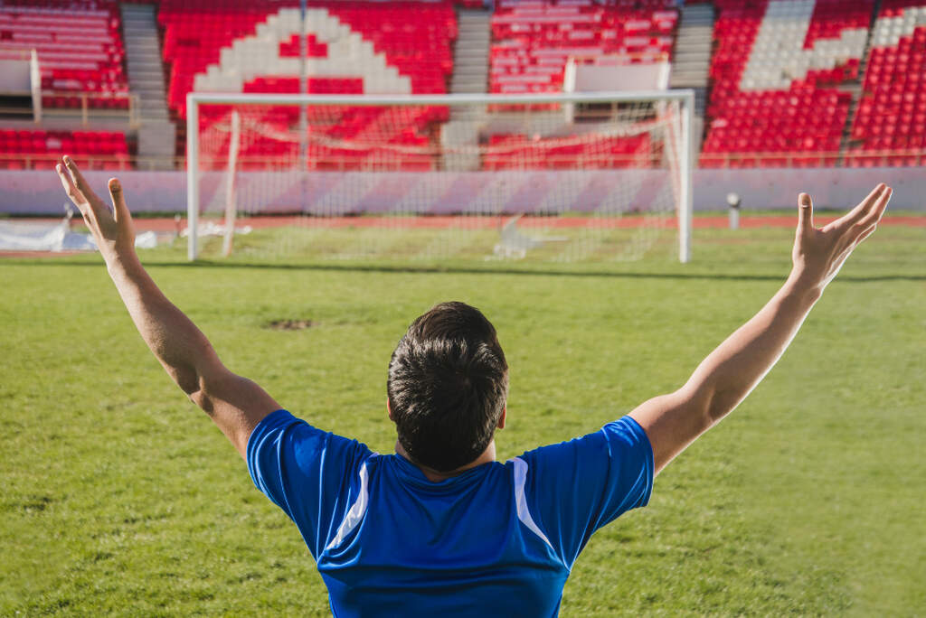 um jogador de futebol ajoelhado no campo e de frente para o gol, sabendo como apostar em um gol de fora da área