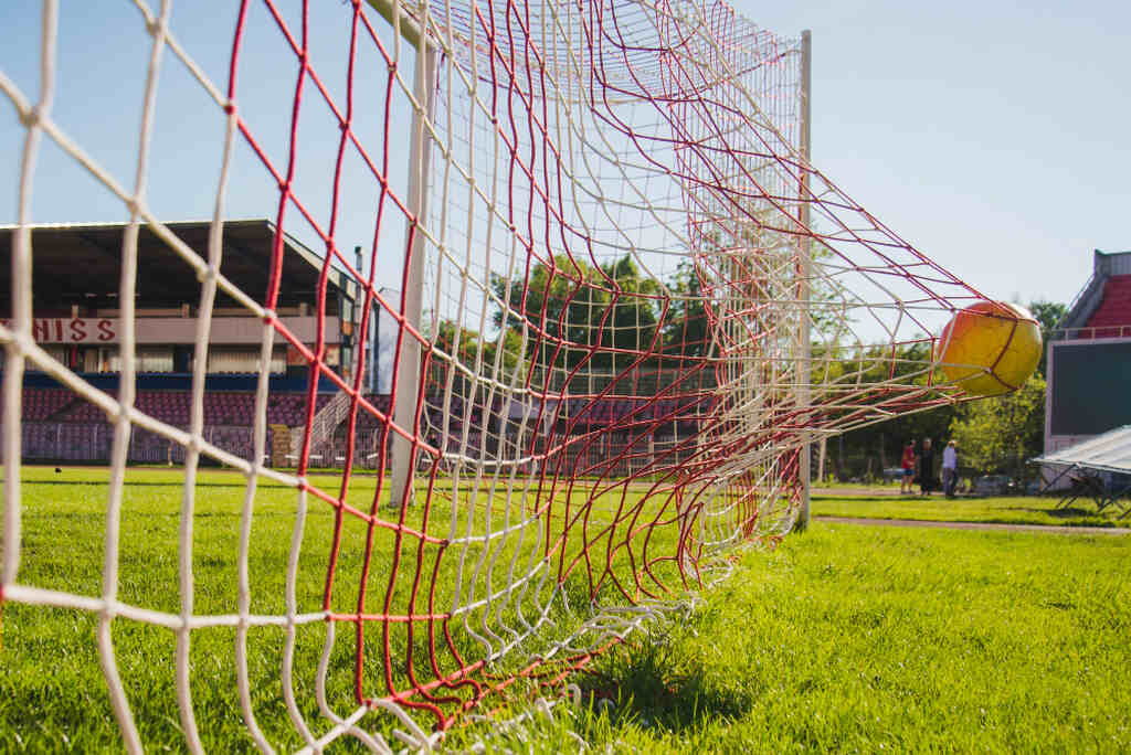 uma bola de futebol batendo a rede, representando como apostar em gol de fora da aréa