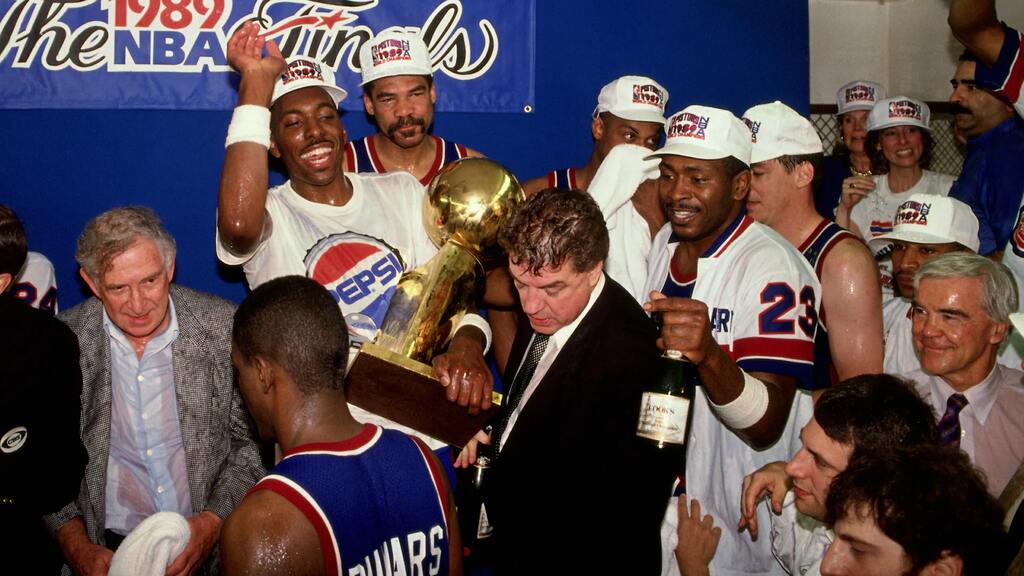 parte do elenco do detroit pistons historia comemorando o titulo da nba com champagne e o trofeu