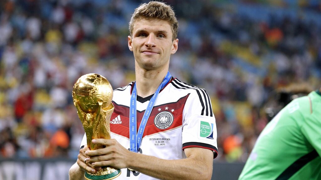 thomas mullher segurando a taça da copa do mundo em campo pela seleção da alemanha. ele é um dos Jogadores com mais assistências na história do futebol​